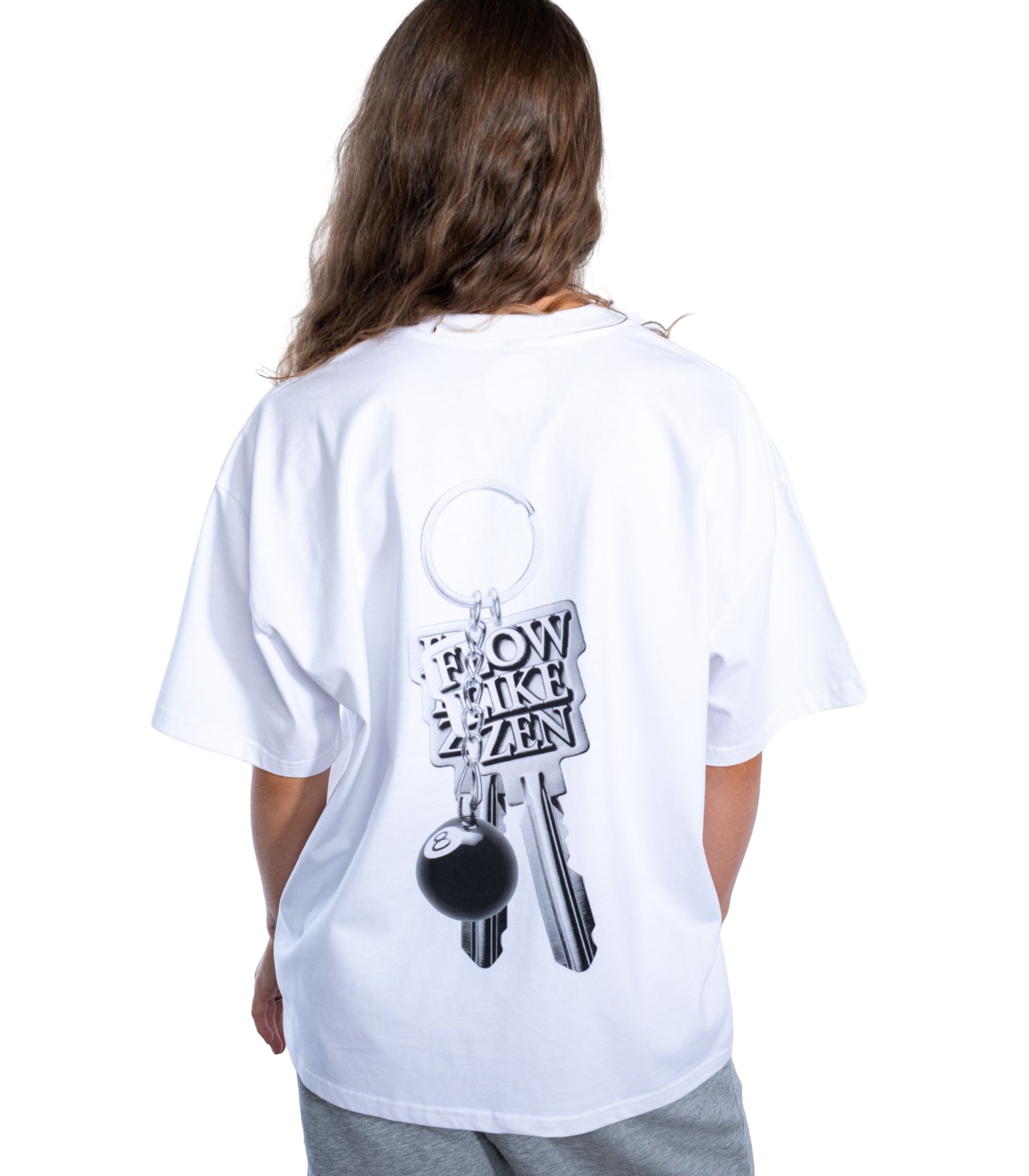 Back view of woman wearing oversized white Flow Like Zen t-shirt with metallic keychain back graphic featuring 8-ball and engraved logo – UK hip-hop and streetwear fashion.