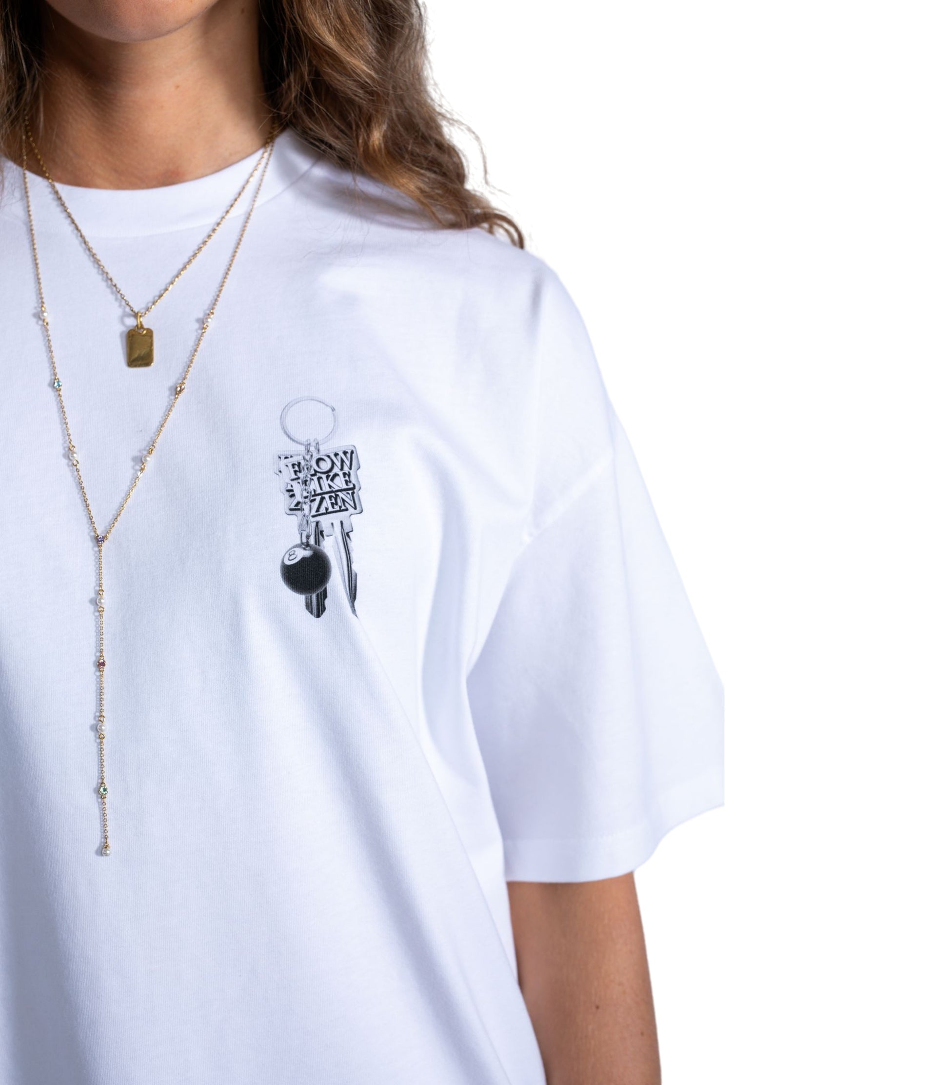 Close-up of white Flow Like Zen t-shirt with small chest print of metallic keychain and 8-ball pendant – UK London streetwear fashion.