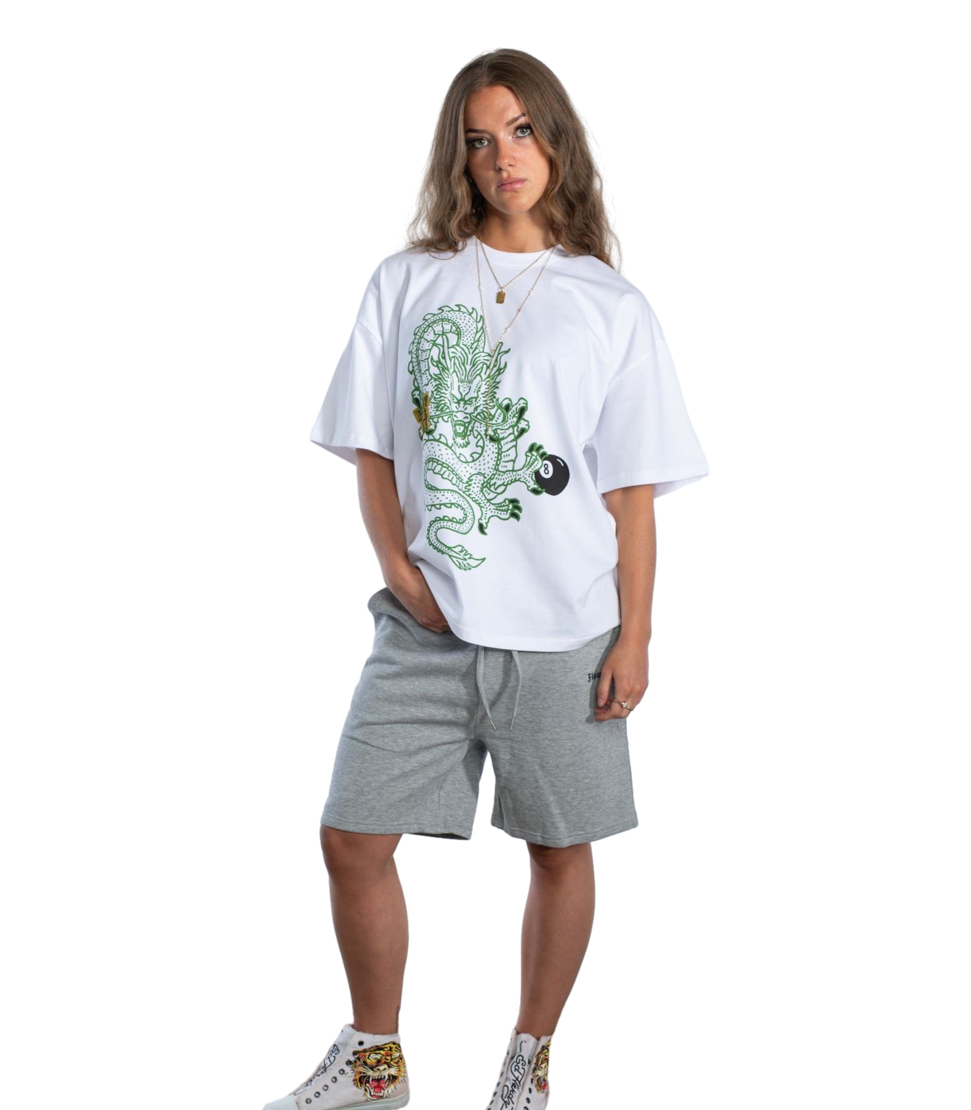 Female model wearing Flow Like Zen’s Dragon’s Grip white t-shirt featuring an intricate green dragon holding a black 8-ball, styled with layered gold necklaces against a plain white backdrop.