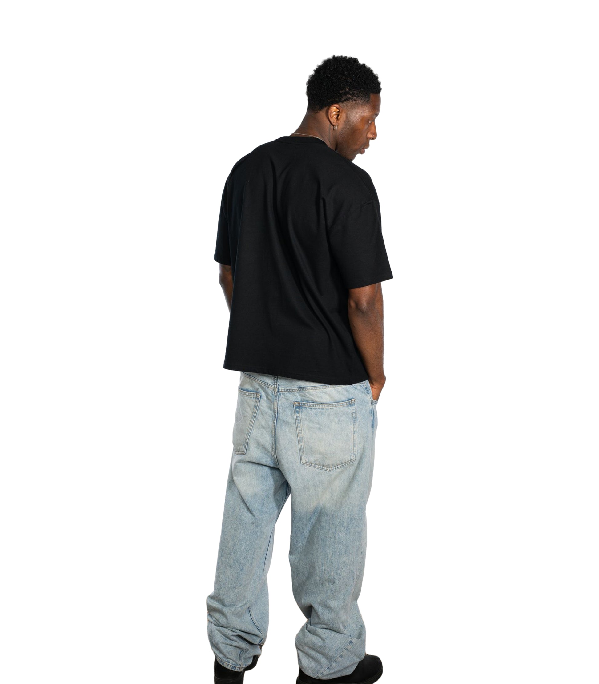 Back view of male model wearing Flow Like Zen black oversized t-shirt and light blue baggy jeans; minimalist British streetwear look with relaxed fit, designed for UK urban fashion culture.