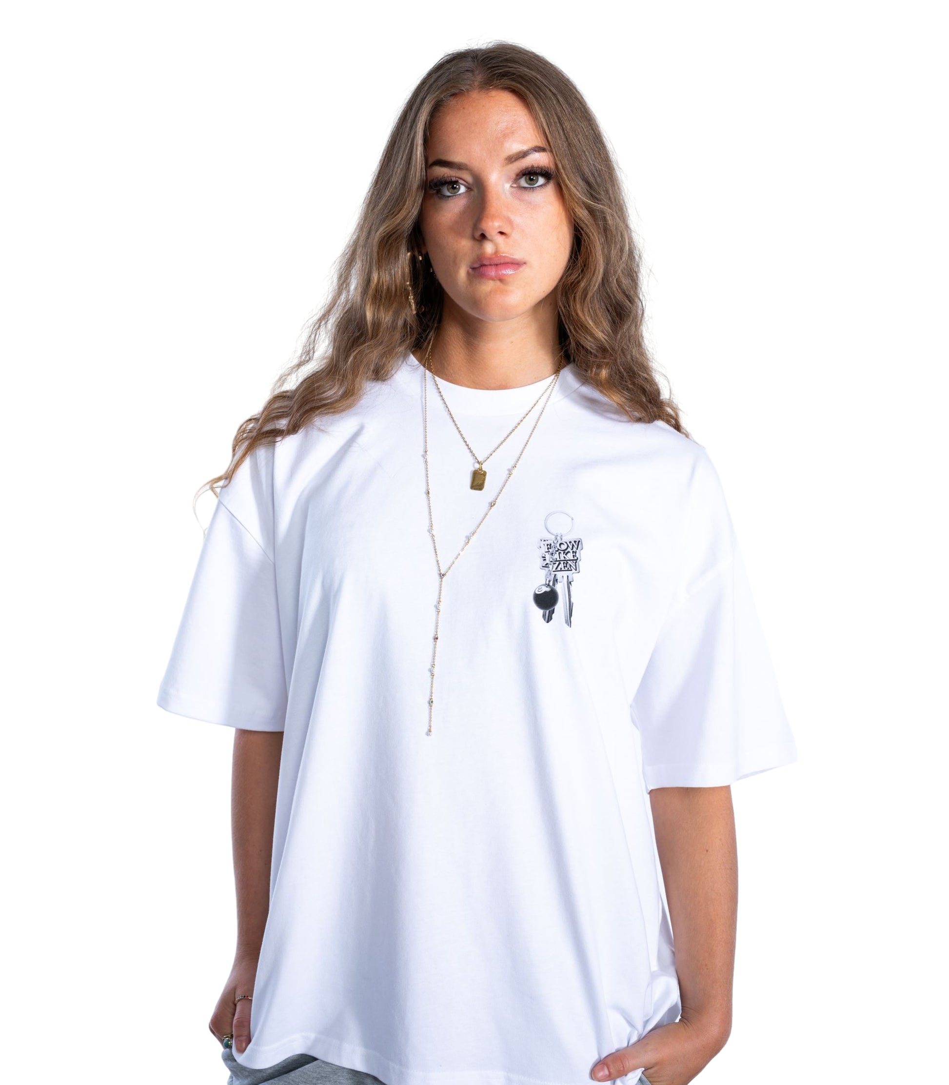 Front view of woman wearing white Flow Like Zen t-shirt with small chest print of metallic keychain and 8-ball – oversized UK streetwear fashion from Manchester.