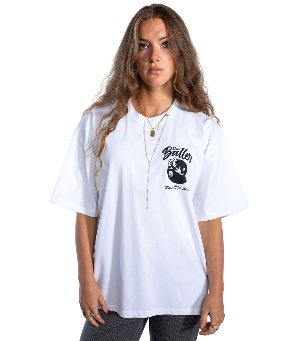 Female model in oversized white UK streetwear t-shirt by Eight Baller, featuring small 8-ball cartoon graphic and 'Flow Like Zen' text – premium British urban fashion