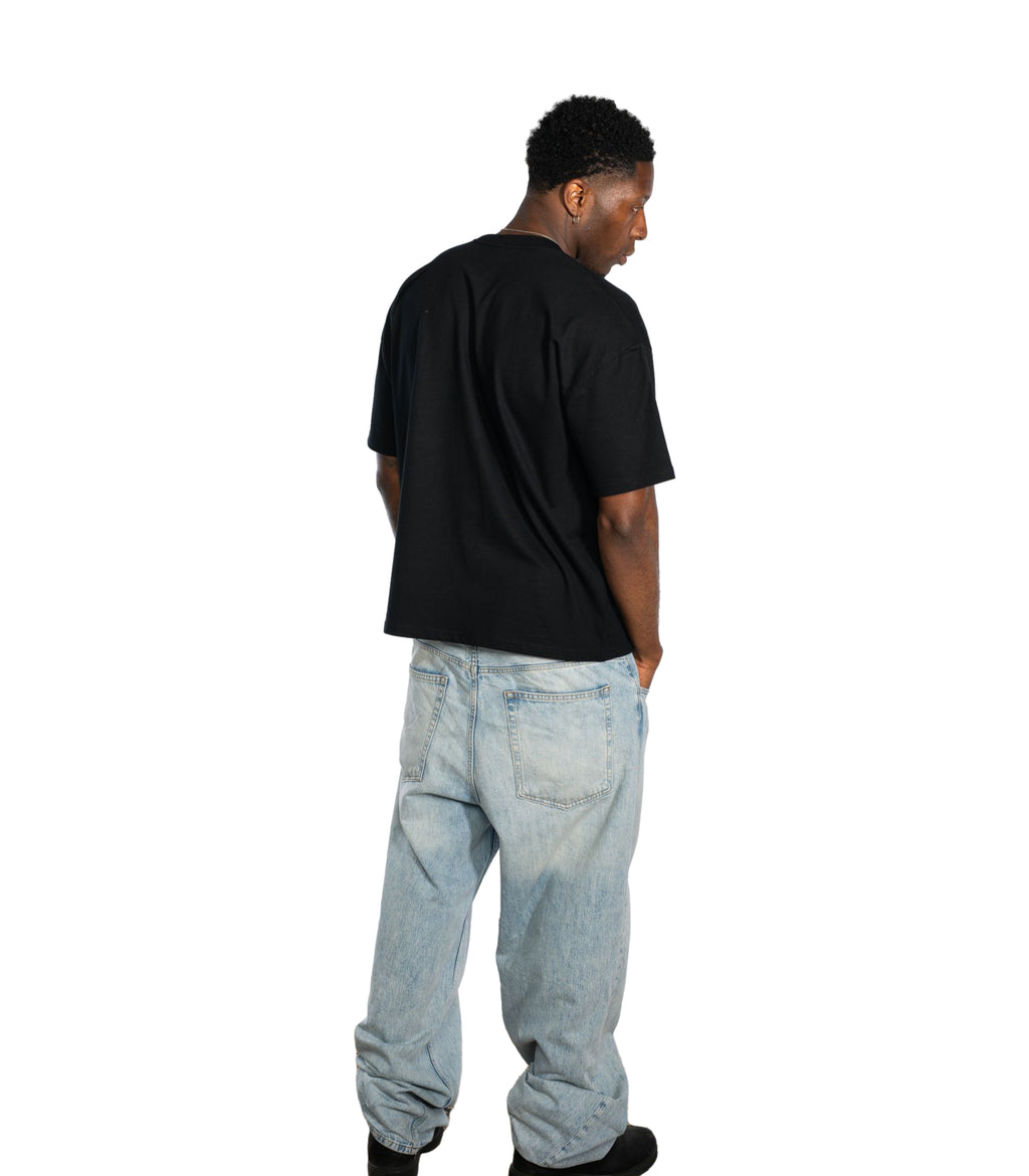 Back view of male model wearing Flow Like Zen black oversized t-shirt and light blue baggy jeans; minimalist British streetwear look with relaxed fit, designed for UK urban fashion culture.